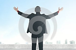 Rear view of Asian businessman standing with raised hand on the rooftop