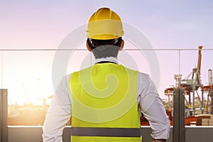 Rear view of an Asian construction worker with hardhat looking at the seaport