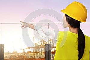 Rear view of an Asian construction worker with hardhat pointing at the seaport