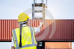 Rear view of asian female engineer in reflective clothing with safety helmet is working and checking at containers cargo on
