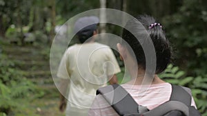 Rear view of Asian female teenager with backpack walking follow her mother during hiking trip in tropical rainforest.