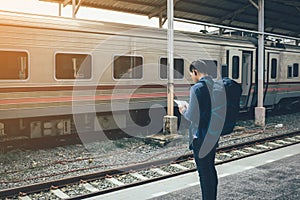 Rear view of asian man waiting train at platform and holding tablet