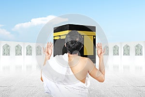 Rear view of Asian Muslim man in ihram clothes standing and praying in front of the Kaaba
