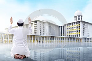 Rear View of Asian Muslim man sitting in pray position while raised hands and praying