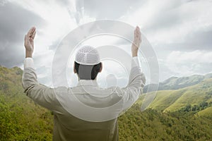 Rear view of Asian Muslim man standing while raised hands and praying