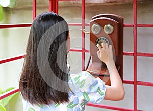 Rear view of Asian young girl kid using dial telephone booth. Child call on the retro vintage red phone booth
