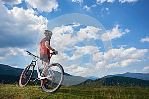 Rear view of athletic sportsman cyclist in sportswear and helmet standing with cross country bike