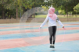Rear view athletic young asian muslim woman in sportswear standing and  skipping rope outdoor for morning exercise. Active girl