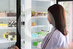 Rear view of attractive asian female smile choosing cake at bakery store