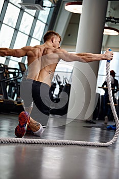 Rear view of Attractive young fit and toned sportswoman working out with battle ropes. Motion blur