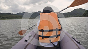 Rear view of attractive young woman rowing on an inflatable kayak on water of large mountain lake. Travel destinations, adventure,