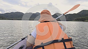 Rear view of attractive young woman rowing on an inflatable kayak on water of large mountain lake. Travel destinations, adventure,