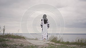 Rear view at awe African American woman wearing long summer fashion dress walking on the field on the background of a