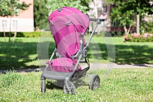 Rear view of baby pushchair folded in seated position on green meadow in summer sunny park, an infant perambulator series