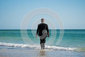 Rear view of back business man in suit in sea water at beach. Businessman tourist in casual suit barefoot walking on