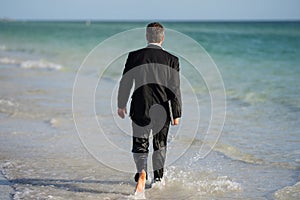 Rear view of back business man in suit in sea water at beach. Handsome business man on summer vacation. Businessman