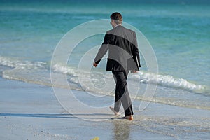 Rear view of back business man in suit in sea water at beach. Remote online working. Crazy summer business. Fun business