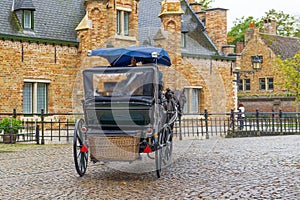 Rear view, back view of horse-drawn carriage goes to the direction of old brick buildings, Bruges, Belgium