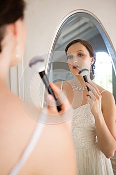 Rear view of beautiful bride applying makeup reflecting on mirror