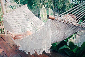 Rear view of beautiful girl in a white hammock in the garden at home. Young woman listening to music & dreaming of summer nature.