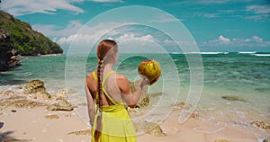 Rear view of beautiful lonely woman with drinking coconut in her hand relaxing on sandy tropical Green Bowl beach