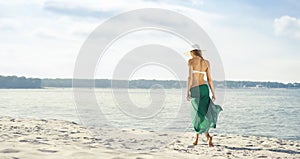 Rear view of beautiful woman in green silk walking along the sea