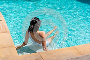 Rear view of beautiful woman in swimsuit relaxing in the pool during her summer holiday. Copy space. Summer and vacation,