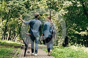 rear view of beautiful young couple in denim shirts with bicycle walking