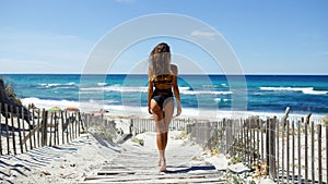 Rear view of a beautiful young woman posing on the beach. Ocean, beach, sand, sky background.