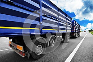 Rear view of the big truck with blue trailer on the countryside road against blue sky with clouds