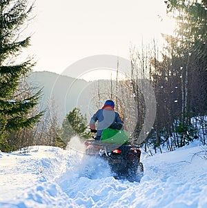 Rear view of a biker driving four-wheeler ATV in winter in the mountains
