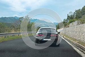 Rear view of a black modified old italian car driving through south Croatia. Crossing a hill with mountains in the distance on a