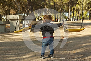 Rear view boy having fun with the swing at the playground