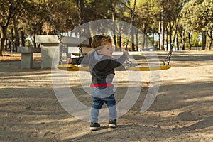 Rear view boy having fun with the swing at the playground