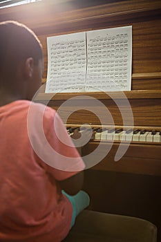 Rear view of boy practising piano in classroom