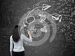 Rear view of a brunette lady who is drawing a graduation sketch. Math formulas, an arrow and geometric figures are drawn on the bl