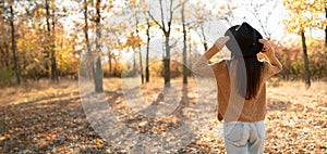 Rear view of a brunette woman in a hat against the background of an autumn forest. Leisure concept