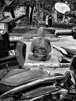 Rear view of buddhist meditating between motorbikes in Hanoi Vietnam