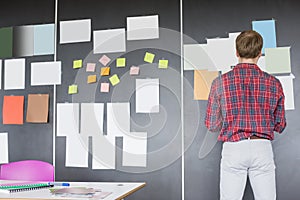 Rear view of businessman analyzing documents on wall at creative office