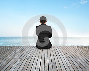 Rear view businessman sitting on wooden floor with sky sea