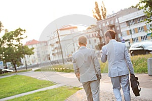 Rear view of businessmen walking at park on sunny day