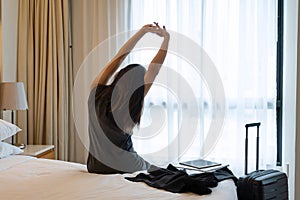 Rear view of businesswoman stretching after check-in at hotel room with luggage and business accessories. Business trip concept