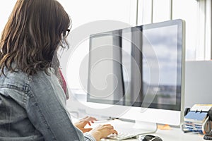 Rear view of businesswoman using desktop computer in creative office