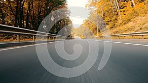 Rear view of a car on an asphalt road in an autumn forest. Fast car driving in slow motion.