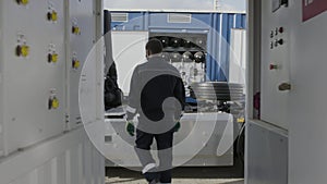 Rear view of a car mechanic in overalls walking through a small corridor to the repair shop. Scene. Professional