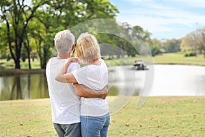 Rear view of caucasian elderly couple lookging at sky with white shirt and blue jean embracing in park in summter time