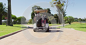 Rear view of caucasian senior couple driving a golf cart with clubs on the back at golf course