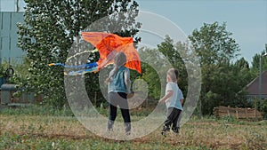 Rear view children play with a kite, a little girl and a boy let a flying snake in the meadow. Happy and carefree