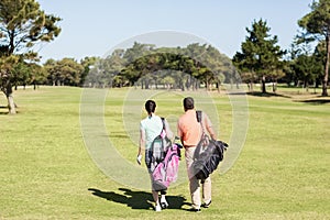 Rear view of couple carrying golf bags
