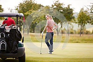 Rear View Of Couple Getting Out Of Golf Buggy To Play Shot On Green